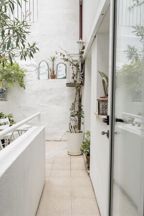 Un pasillo estrecho con plantas en macetas, una pared blanca y una puerta que da a una habitación.