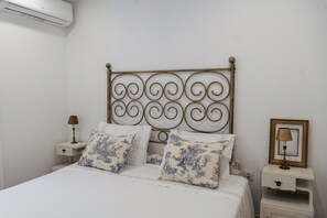 Quarto com cama, cabeceira decorativa, mesas de cabeceira e ar condicionado fixado na parede.