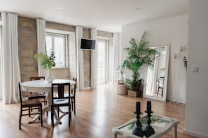 Un coin repas avec une table ronde, des chaises, un téléviseur fixé au mur et une grande plante en pot.