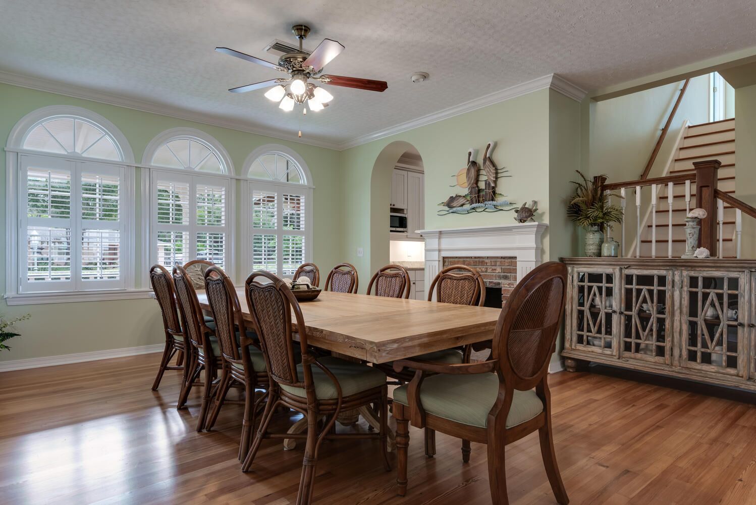 A dining room with a wooden table and chairs, a ceiling fan, and a fireplace.