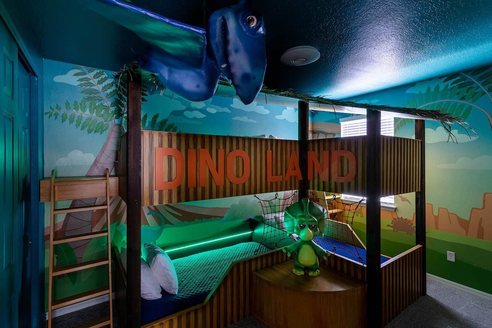 A children's playroom with a dinosaur theme, including a bed, a hanging dinosaur, and a mural.