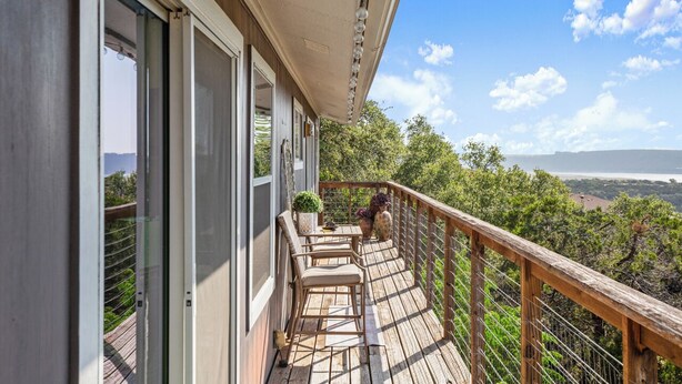 A wooden deck with outdoor seating, a railing, and a view of trees and distant landscape. - Lake Travis Premium - Austin Views with Great Reviews (Austin)