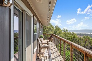 A wooden deck with outdoor seating, a railing, and a view of trees and distant landscape.
