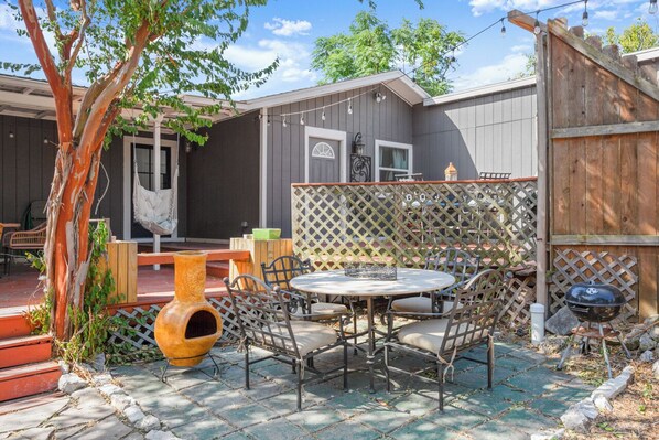 An outdoor patio with a round table and chairs, a hammock, and a wooden fence.