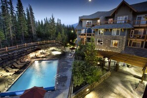 A two-story building with a stone facade, a swimming pool with lounge chairs, and a wooden deck. - Spacious two-bedroom retreat in the heart of Canmore (Canmore)