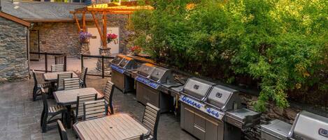 An outdoor patio with stone walls, a pergola, and a row of barbecue grills.