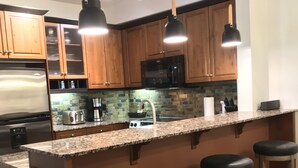 Una cocina moderna con armarios de madera, encimera de granito y electrodomésticos de acero inoxidable, además de taburetes de bar.