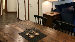 Un comedor con una mesa de madera, sillas y una lámpara con un diseño único de asta de ciervo. Hay cuadros en la pared y una lámpara sobre una mesita auxiliar.