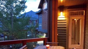 Una terraza de madera con una mesa y sillas, con vistas a una montaña y otros edificios.