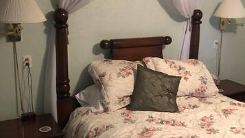 A bedroom with a four-poster bed, floral bedding, two bedside lamps, and a nightstand with drawers.