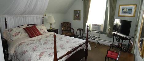 A bedroom with a four-poster bed, a desk with a computer, a chair, and a television.