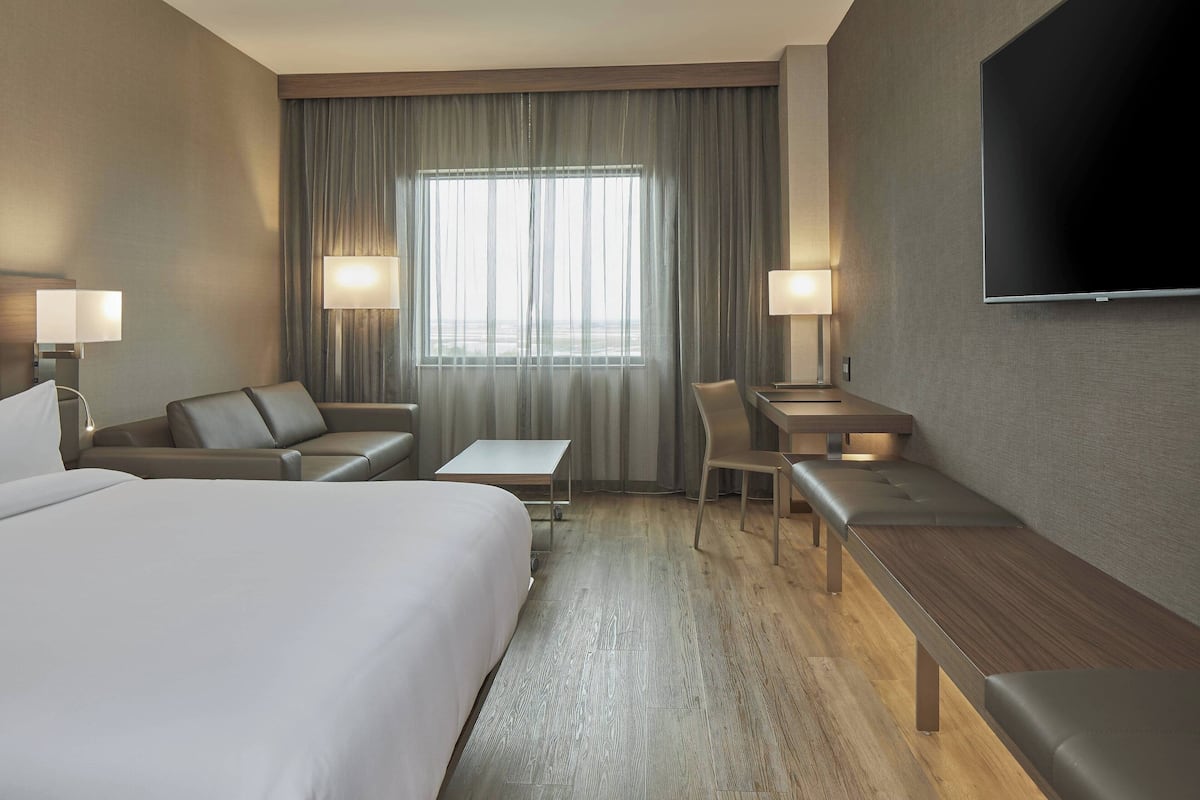 Een hotelkamer met een groot bed, een bureau, een stoel, een bankje en een televisie.