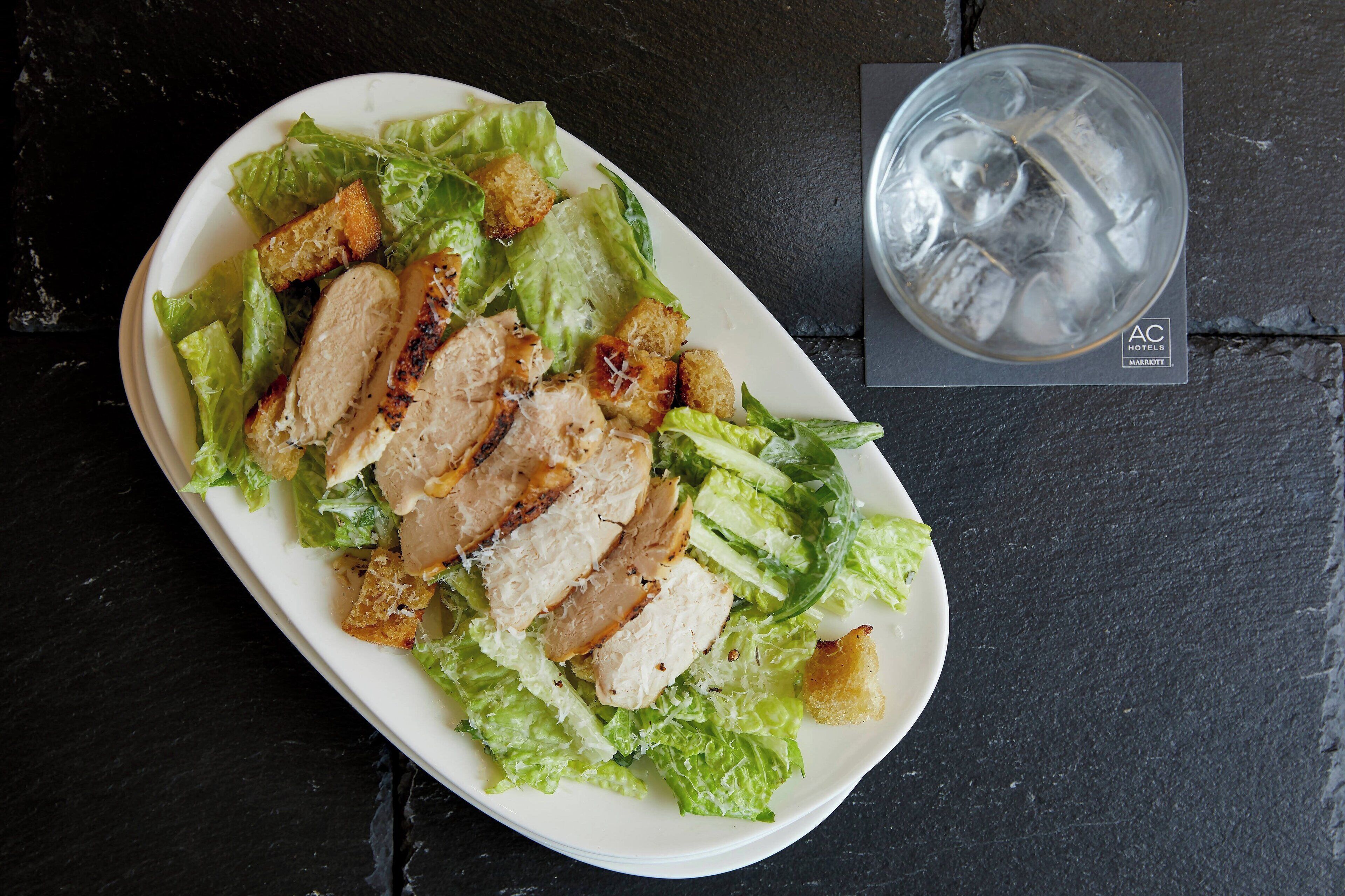 Une assiette de poulet grillé et de salade verte avec des croûtons, servie dans une assiette ovale blanche.