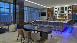 Un hall d’hôtel moderne doté d’un bar, de différents espaces de détente et d’un grand écran de télévision.