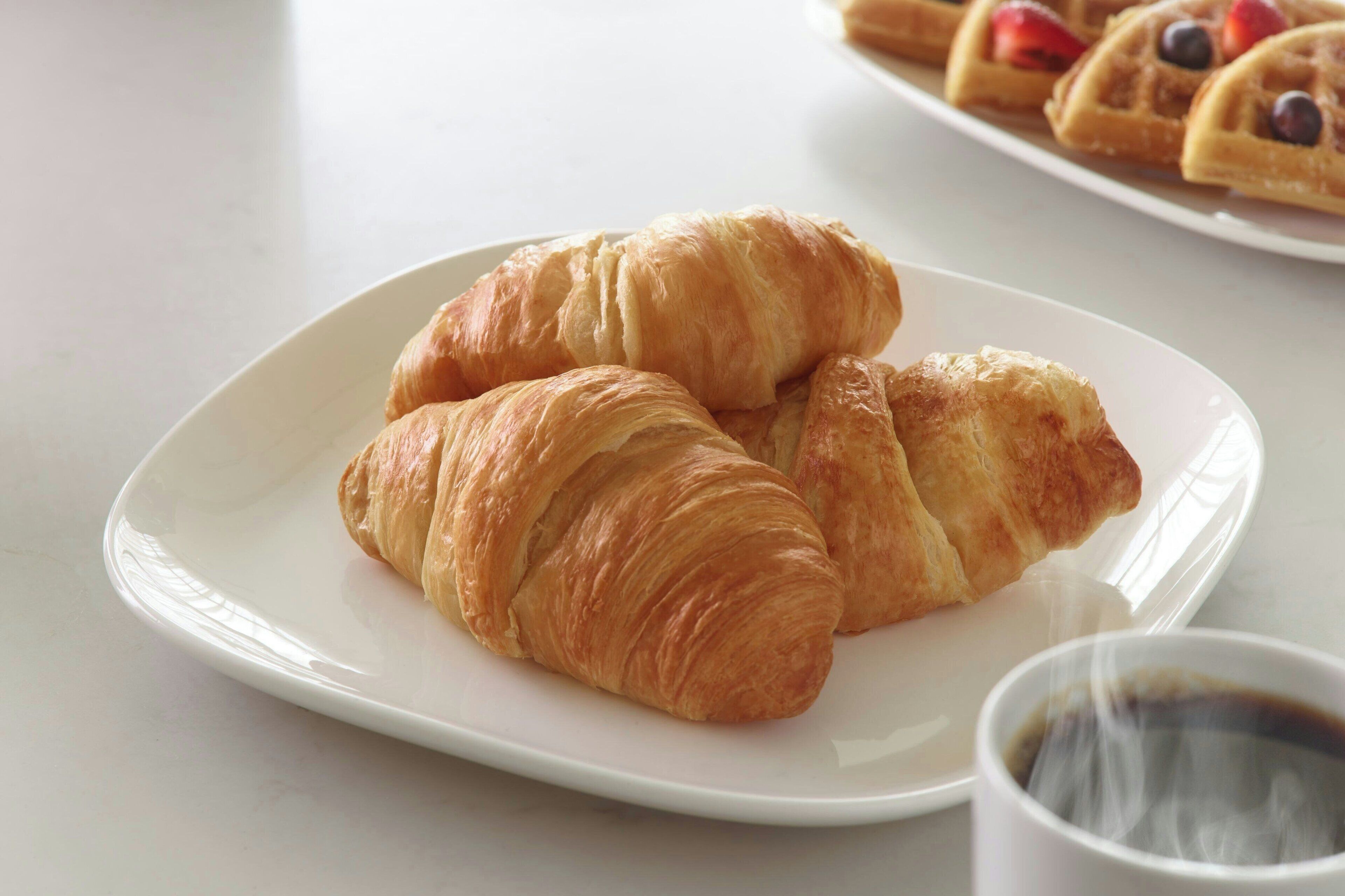 A plate with croissants and a cup of coffee on a white table.