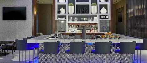 Un espace bar moderne doté d’un îlot central, de tabourets de bar et d’étagères ornées d’objets décoratifs.