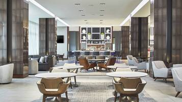 A modern lounge area with round tables and chairs, a bar in the background, and a large window with a view.