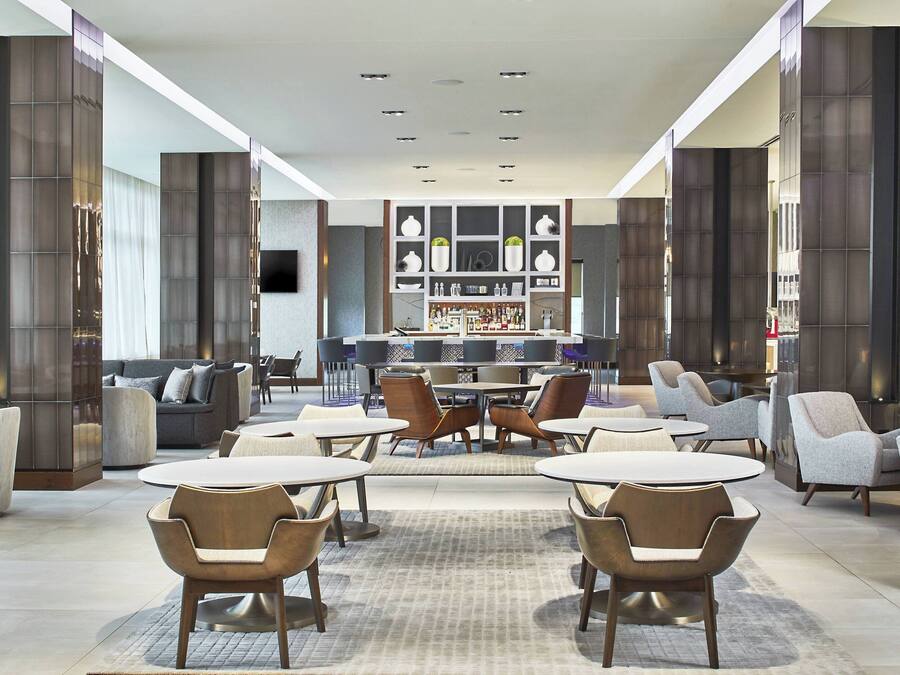 A modern lounge area with round tables and chairs, a bar in the background, and a large window with a view.