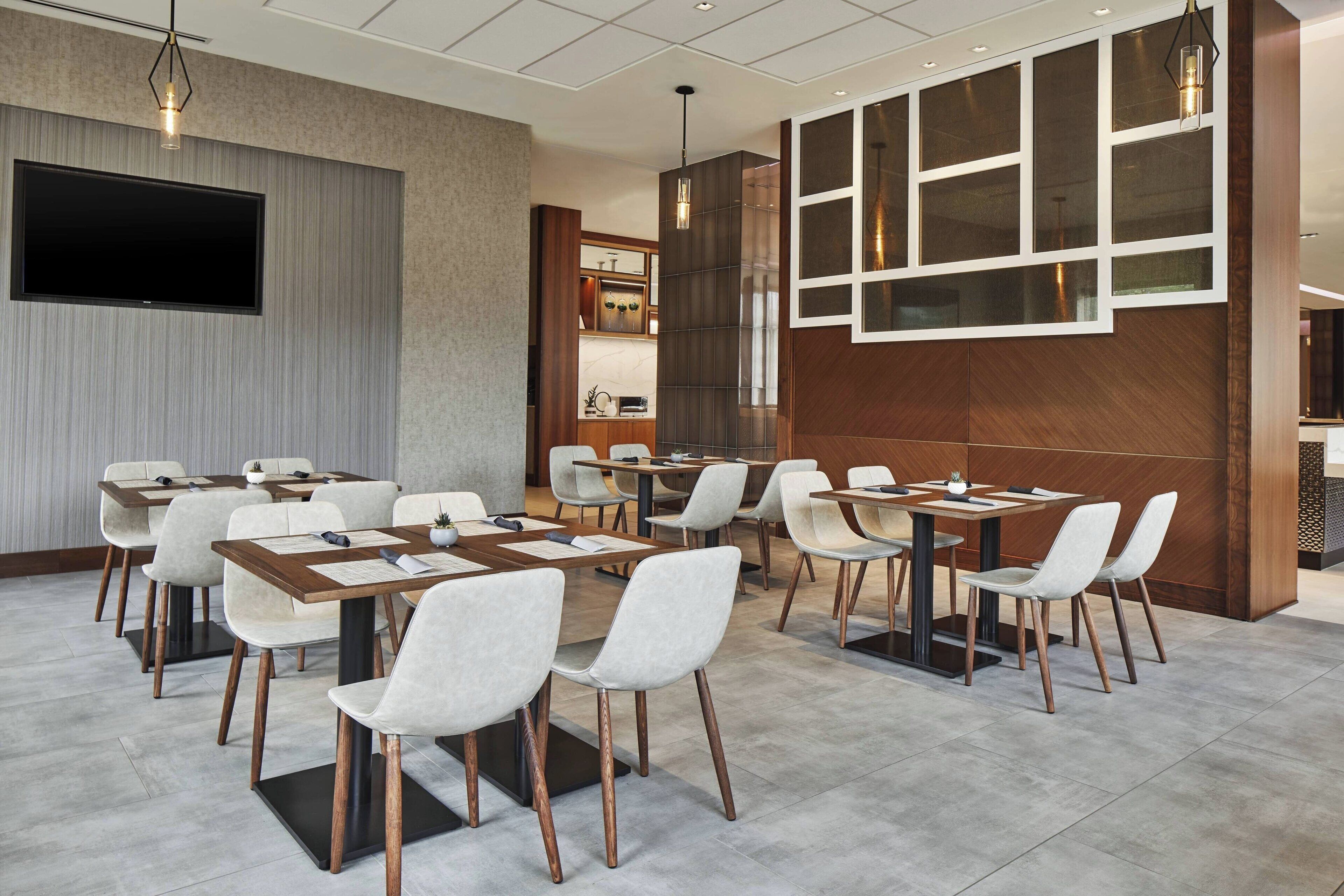 Un salón de conferencias con mesas y sillas, un televisor de pantalla plana y una pared de madera decorativa.