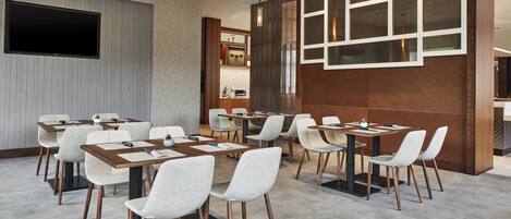 Un salón de conferencias con mesas y sillas, un televisor de pantalla plana y una pared de madera decorativa.