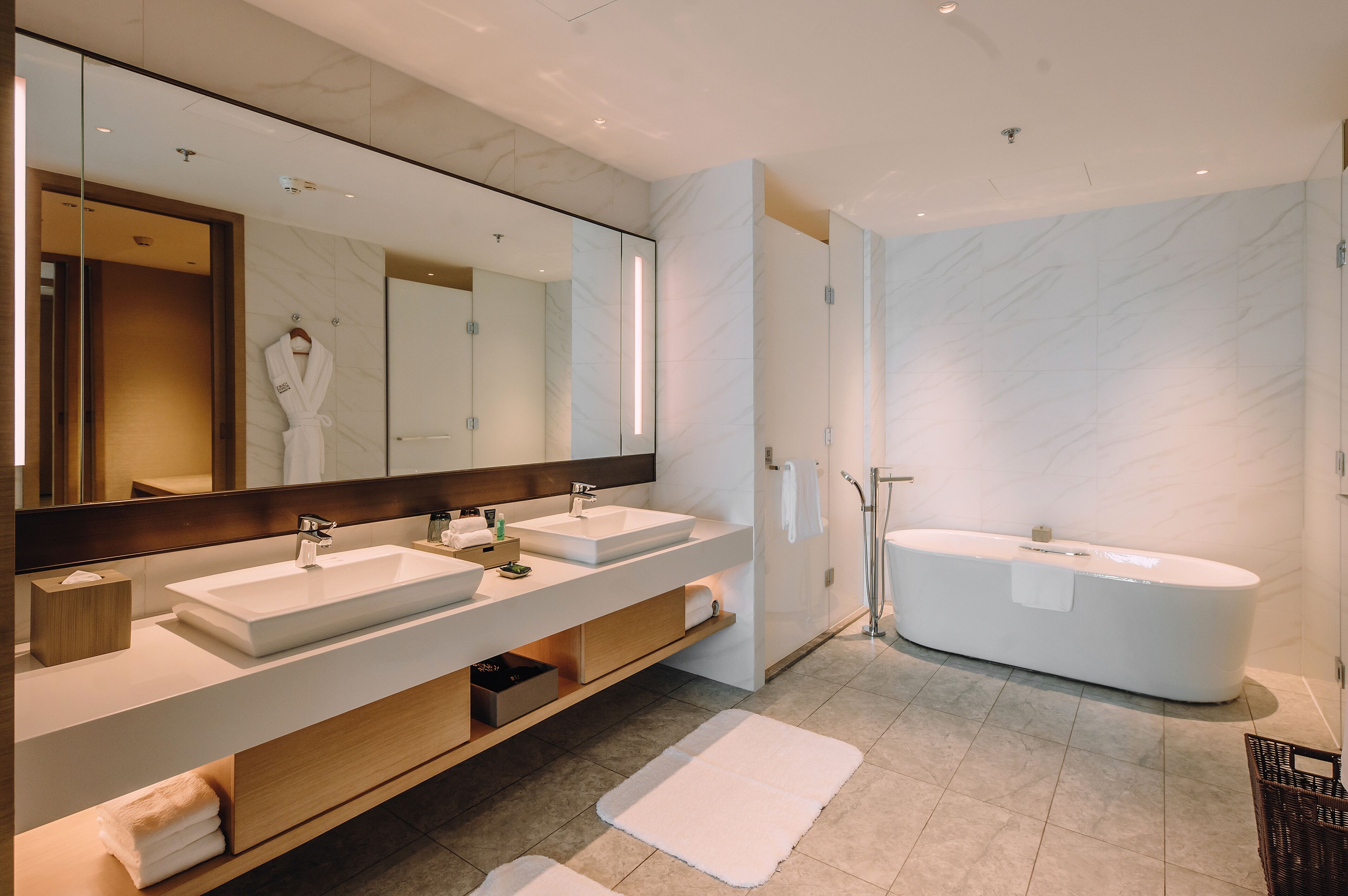 A modern bathroom with two sinks, a large mirror, a bathtub, and a walk-in shower.
