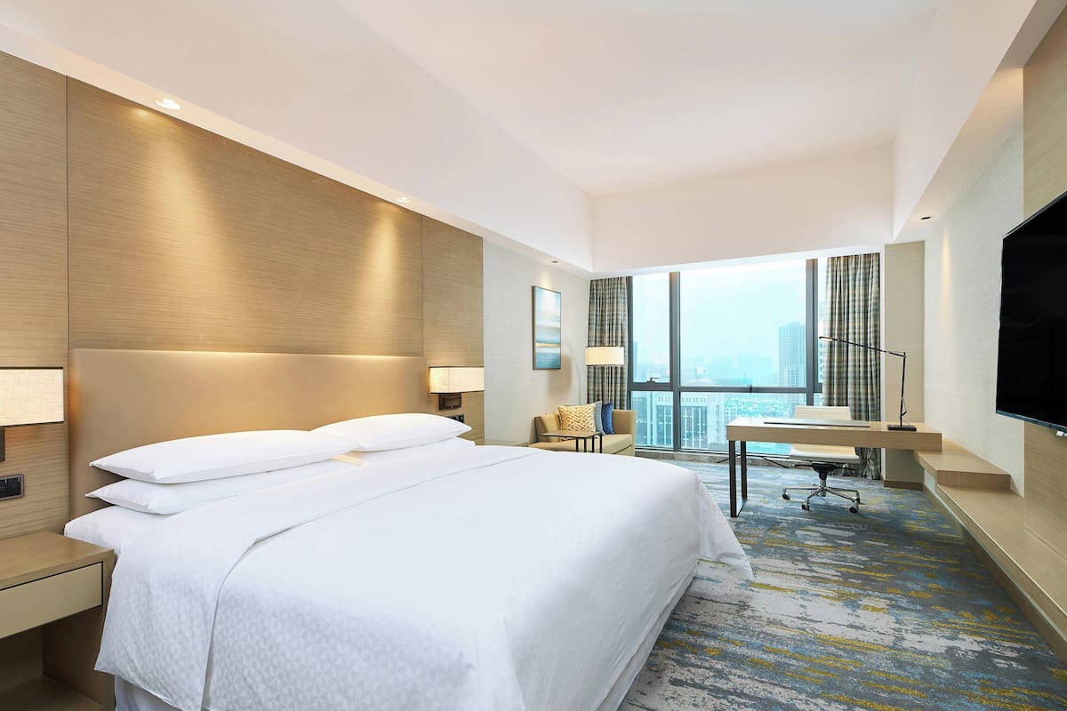 A hotel room with a large bed, a desk, a chair, and a TV.