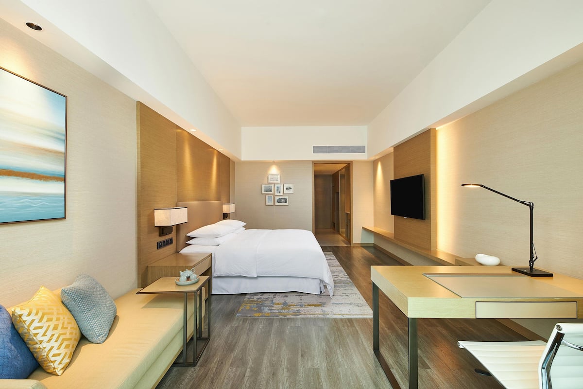 A modern hotel room with a bed, bedside tables, a desk, a TV, and a sofa.