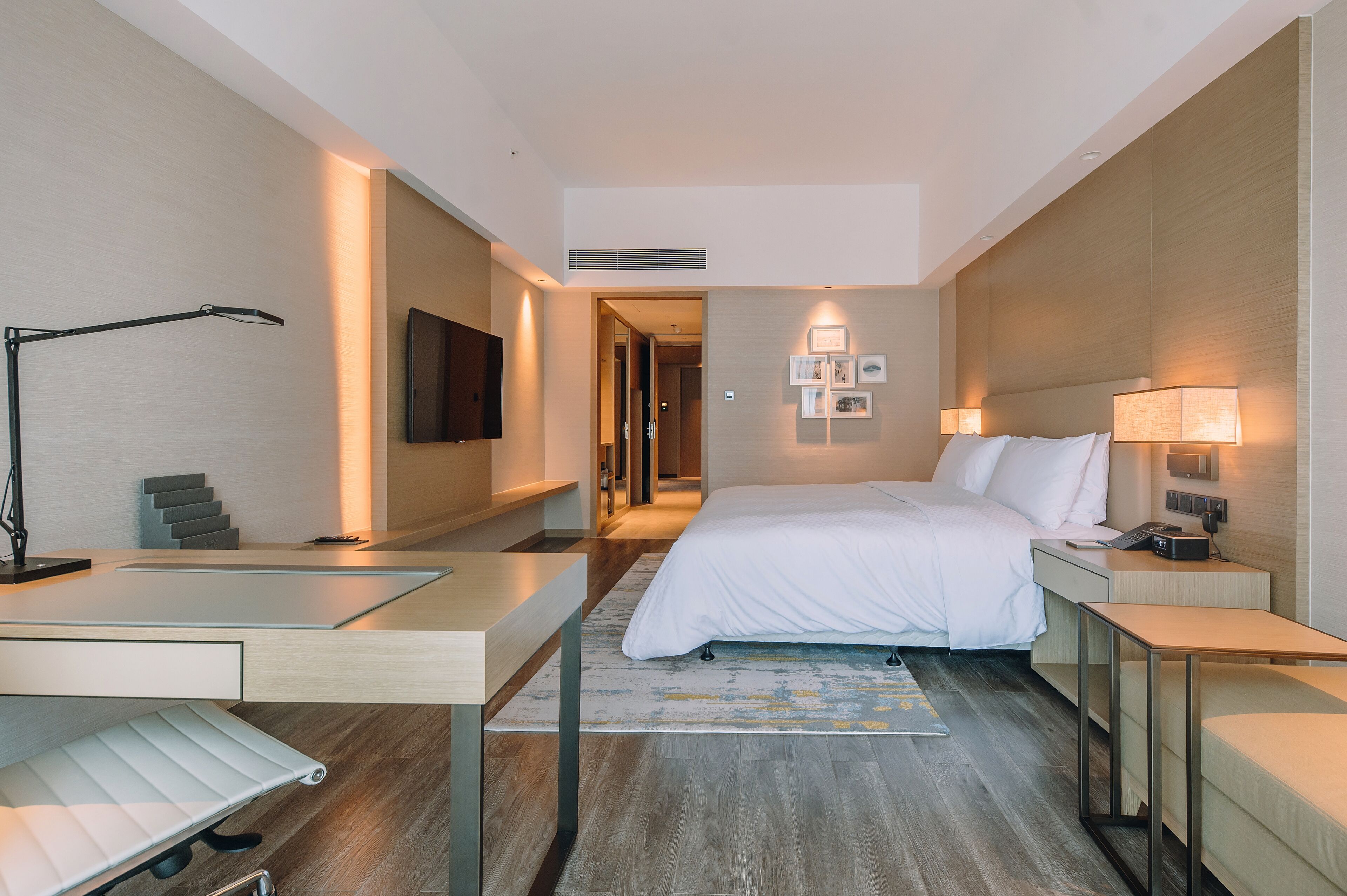 A modern hotel room with a bed, bedside tables, a desk, a chair, and a TV.