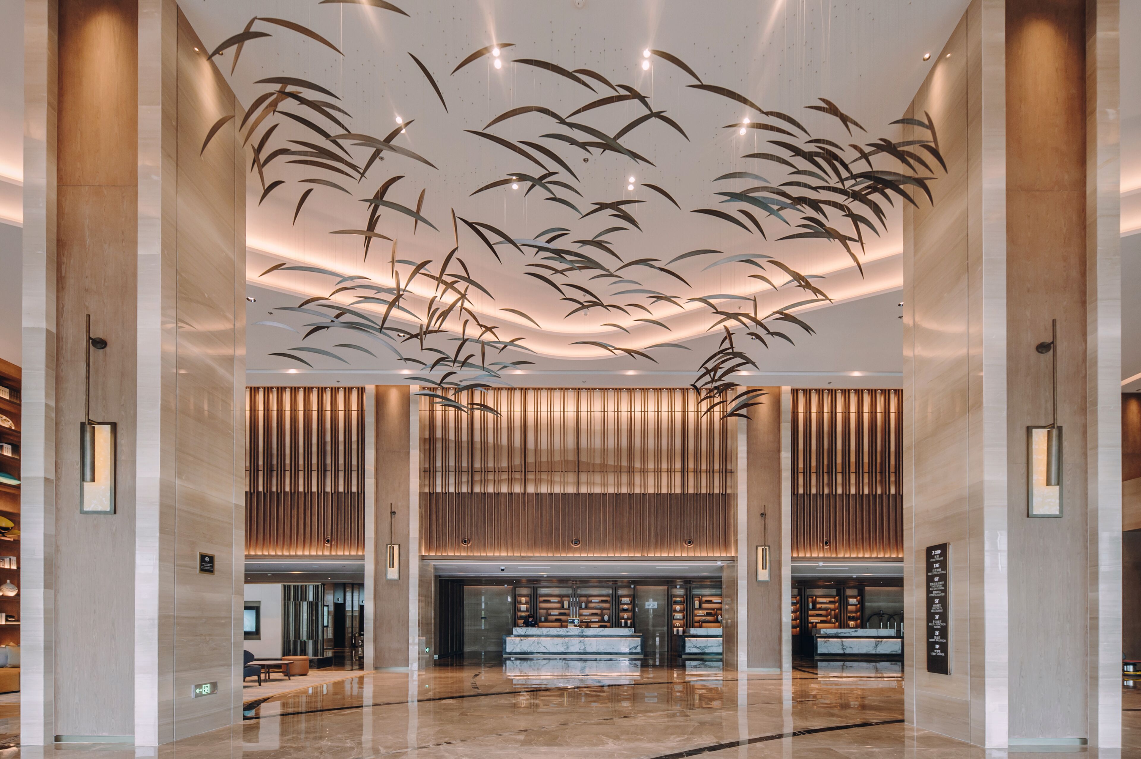 Un hall d’entrée spacieux au design moderne, comprenant un comptoir d’accueil central, des lambris en bois verticaux et des luminaires suspendus.