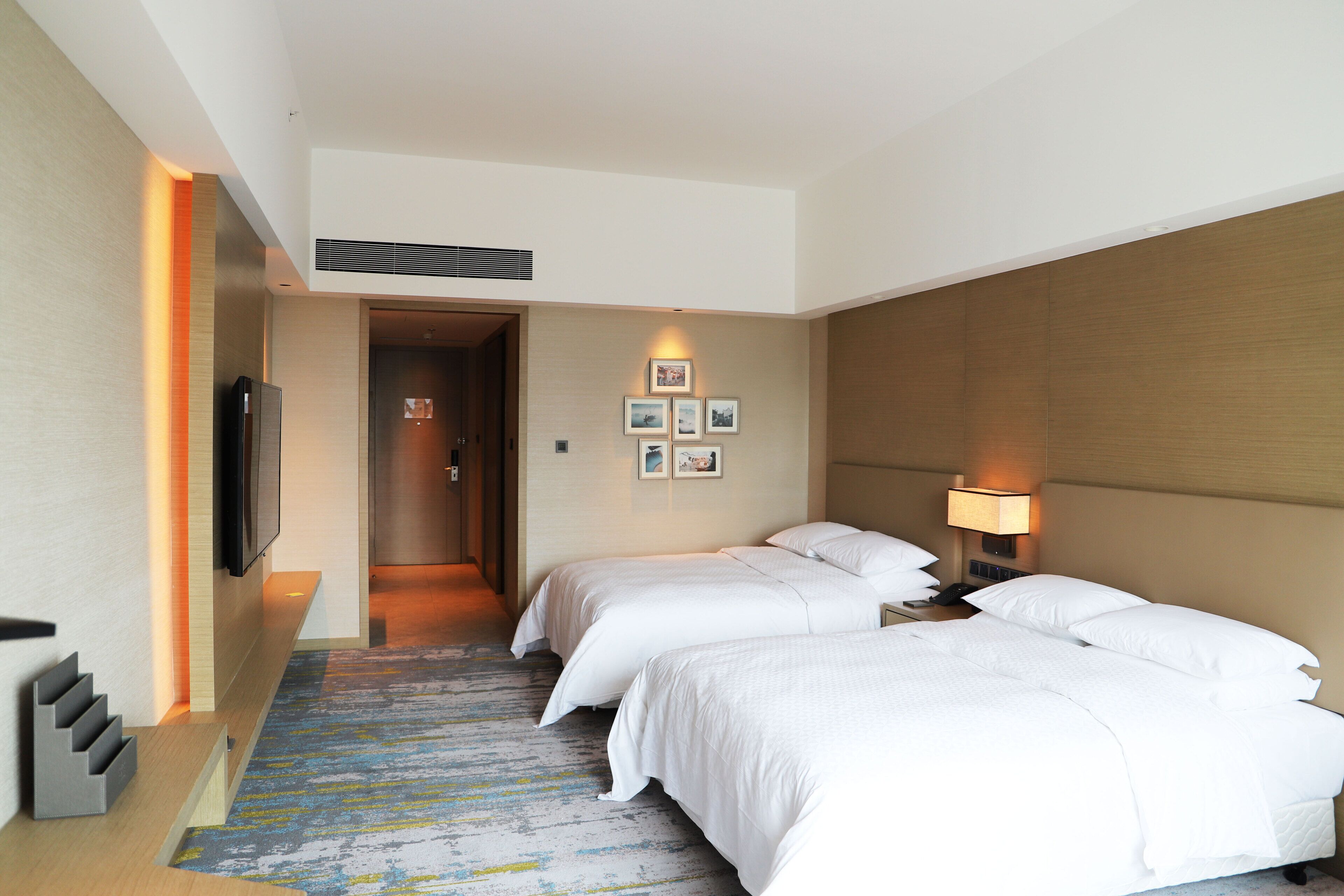 A hotel room with two beds, a TV, a bedside lamp, and a door leading to a hallway.