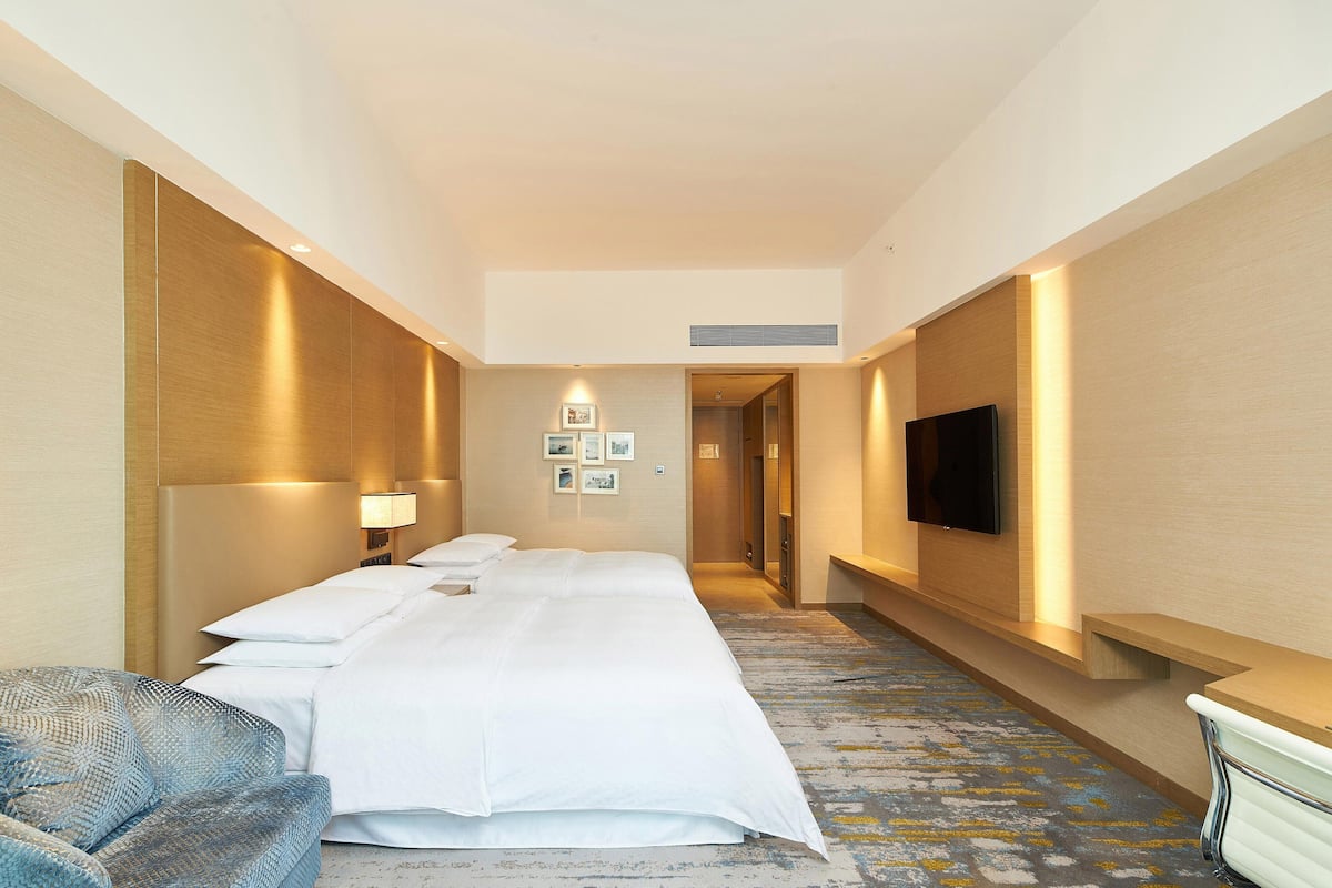A hotel room with a large bed, a bedside table, a TV mounted on the wall, and a small seating area with a chair.