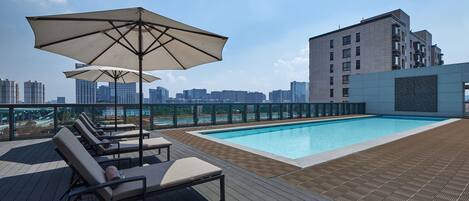 Ein Poolbereich auf dem Dach mit Liegestühlen und Sonnenschirmen, umgeben von einer Stadtansicht.