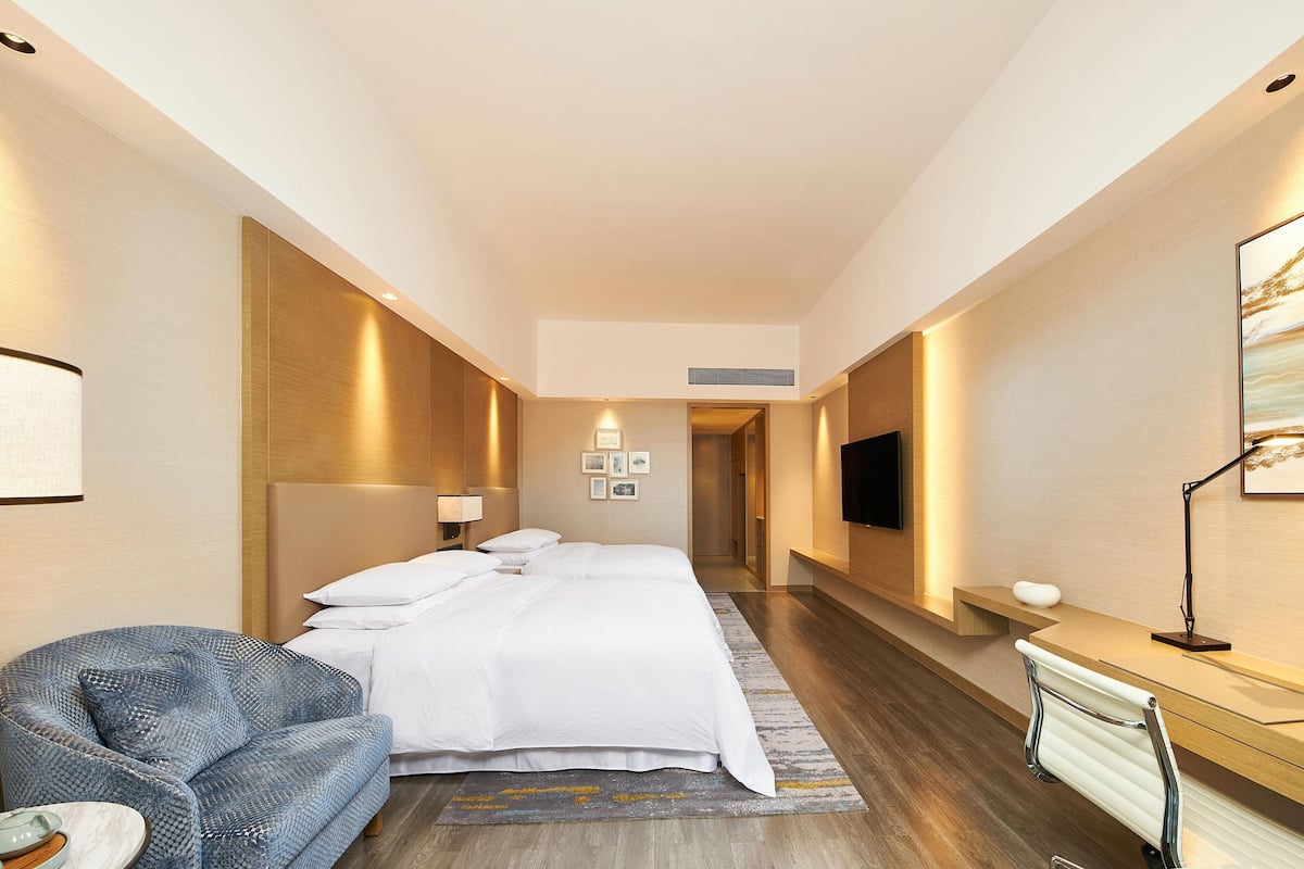 A modern hotel room with a large bed, a seating area, a desk, and a flat-screen TV.