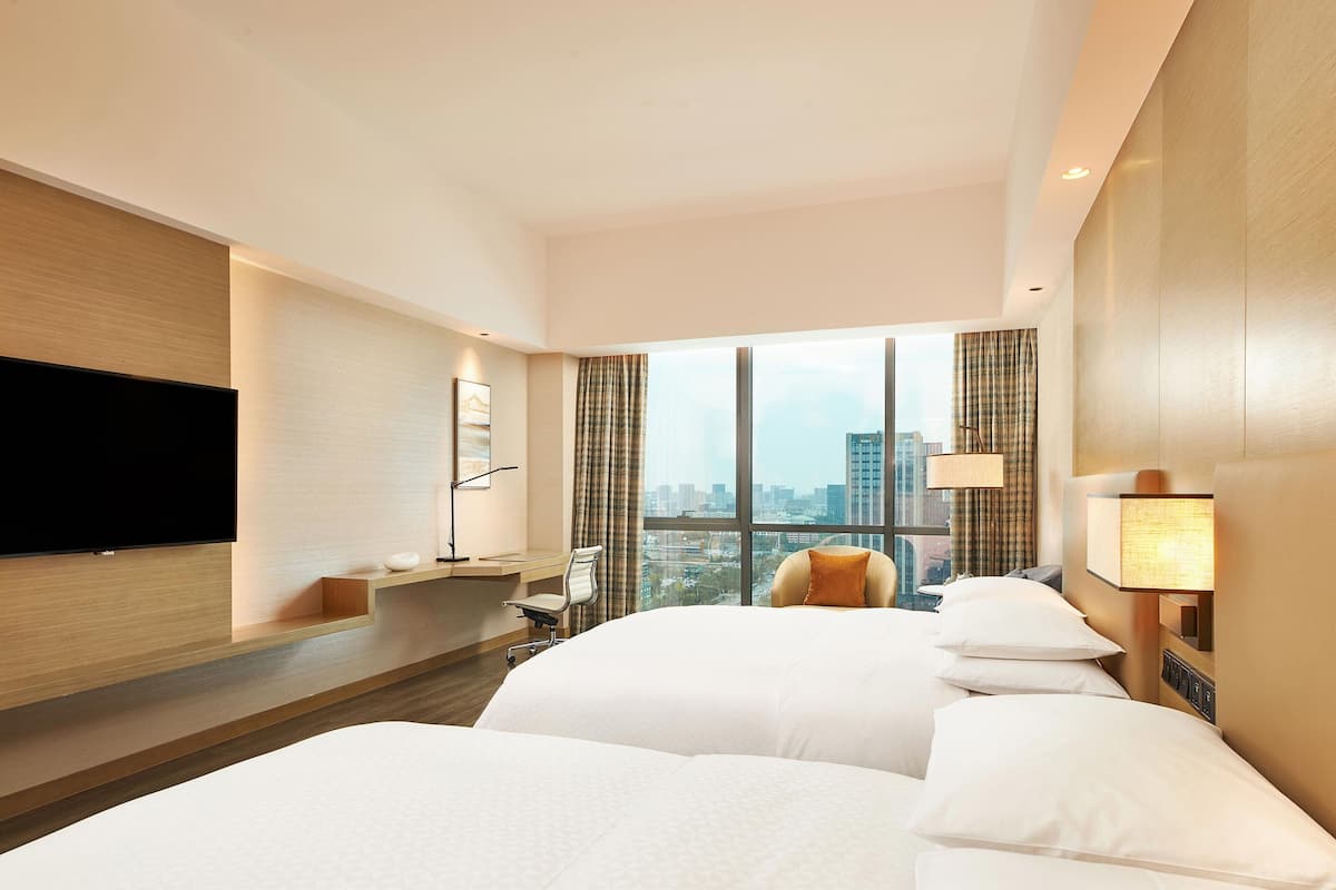 A hotel room with a large bed, a desk, a TV, and a view of the city.
