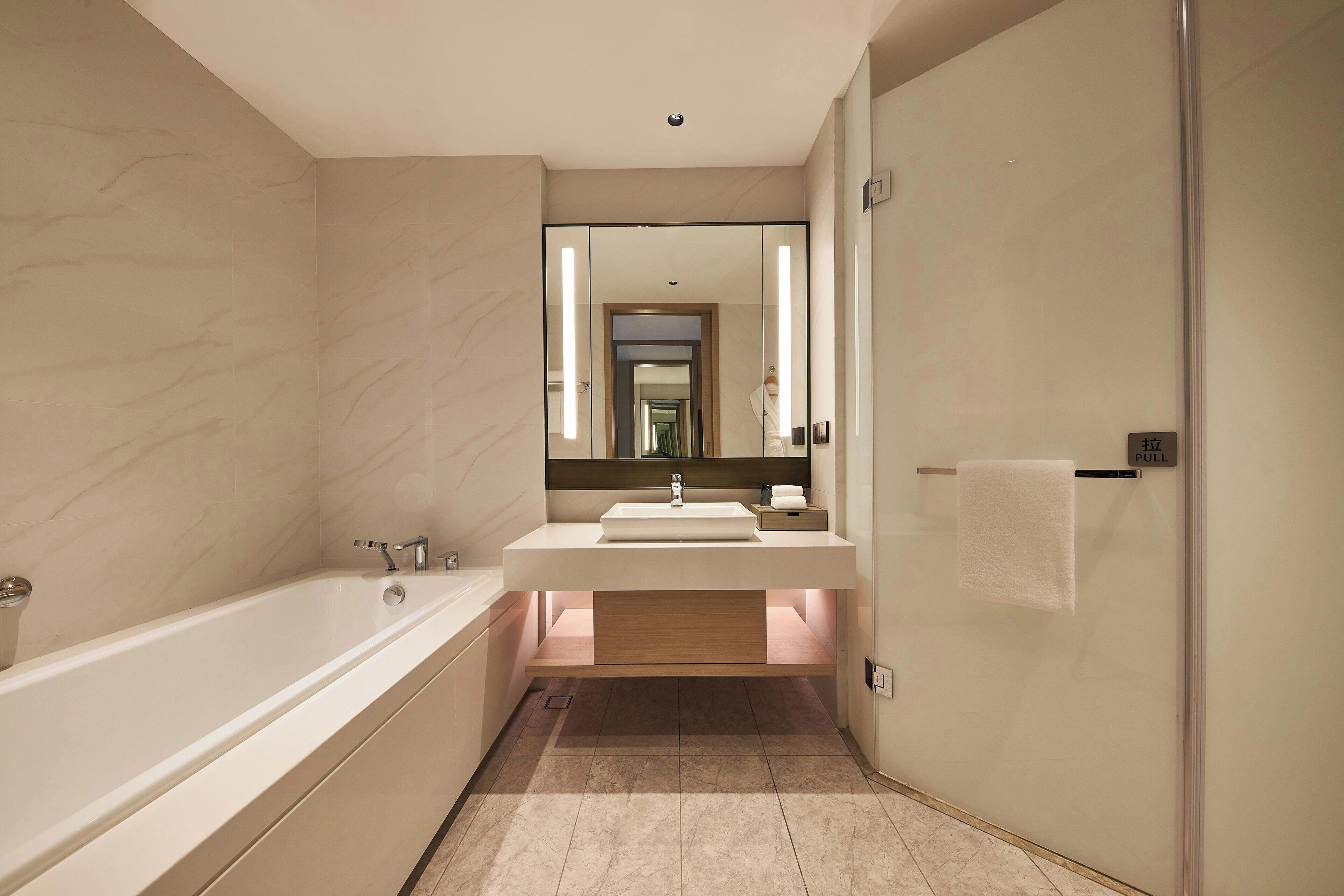 A modern bathroom with a bathtub, vanity with a mirror, and a towel rack.
