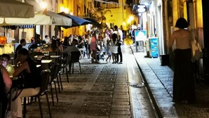 A narrow street lined with buildings, some with outdoor seating and umbrellas, suggesting a dining area.