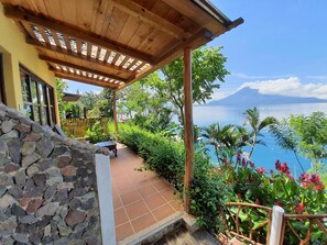 Un espace extérieur abrité, doté d’un mur en pierre, d’une pergola en bois et offrant une vue sur un lac et des montagnes.