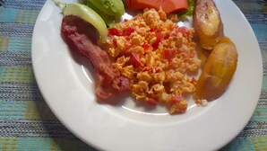 Een bord met roerei, spek, avocado, tomaat, sla en gebakken plantains.