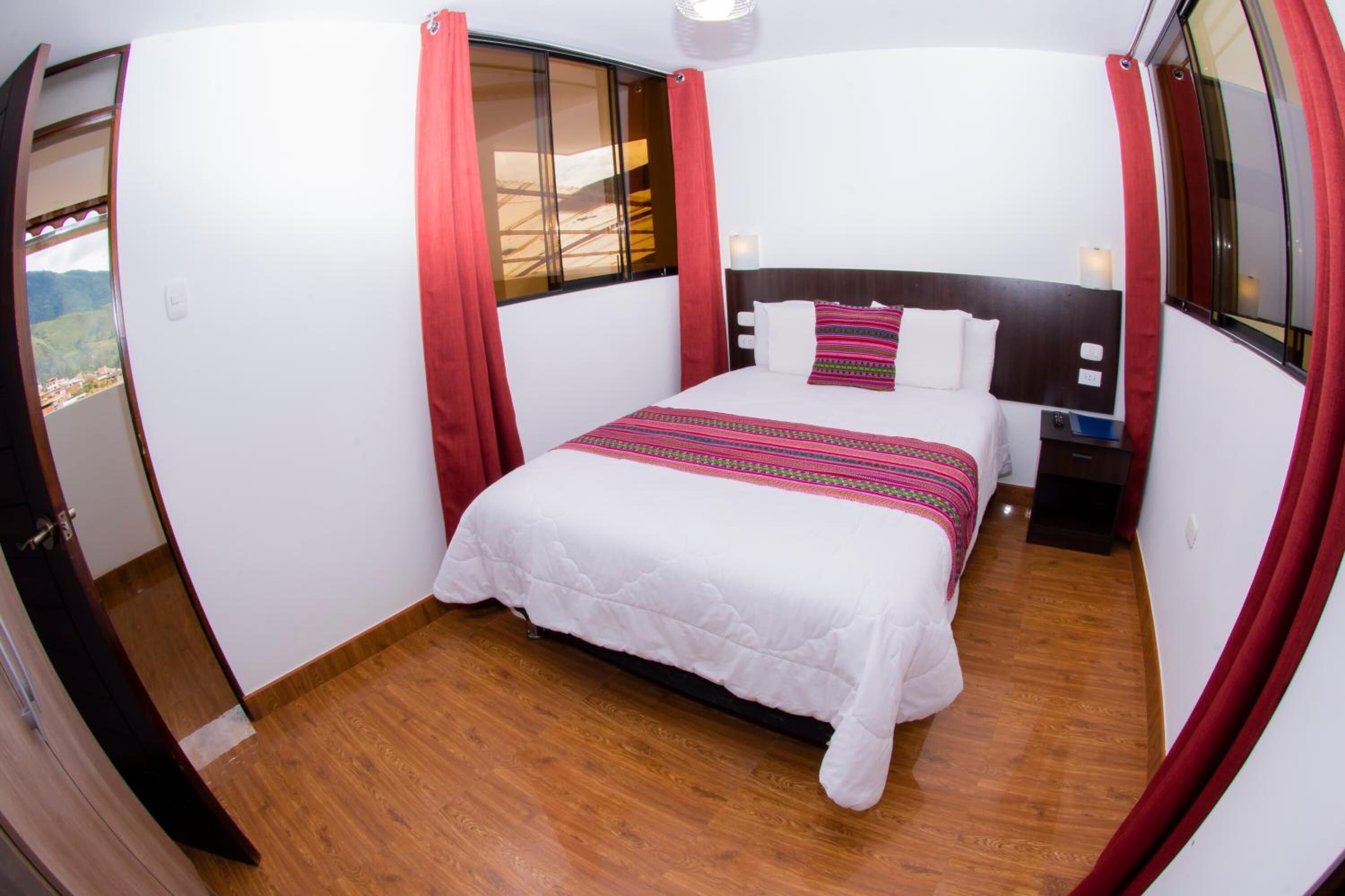 Una camera da letto con un letto, un comodino, una finestra con tende e vista su un paesaggio montuoso.
