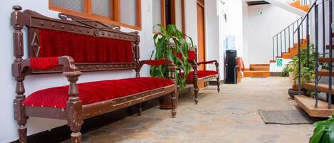 Un banco de madera tradicional con cojines rojos, suelo de losas de piedra y una escalera con escalones de madera y barandillas de metal.