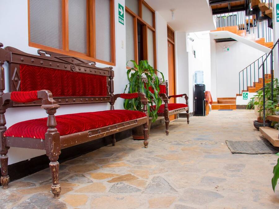 A traditional wooden bench with red cushions, a stone-tiled floor, and a staircase with wooden steps and metal railings.