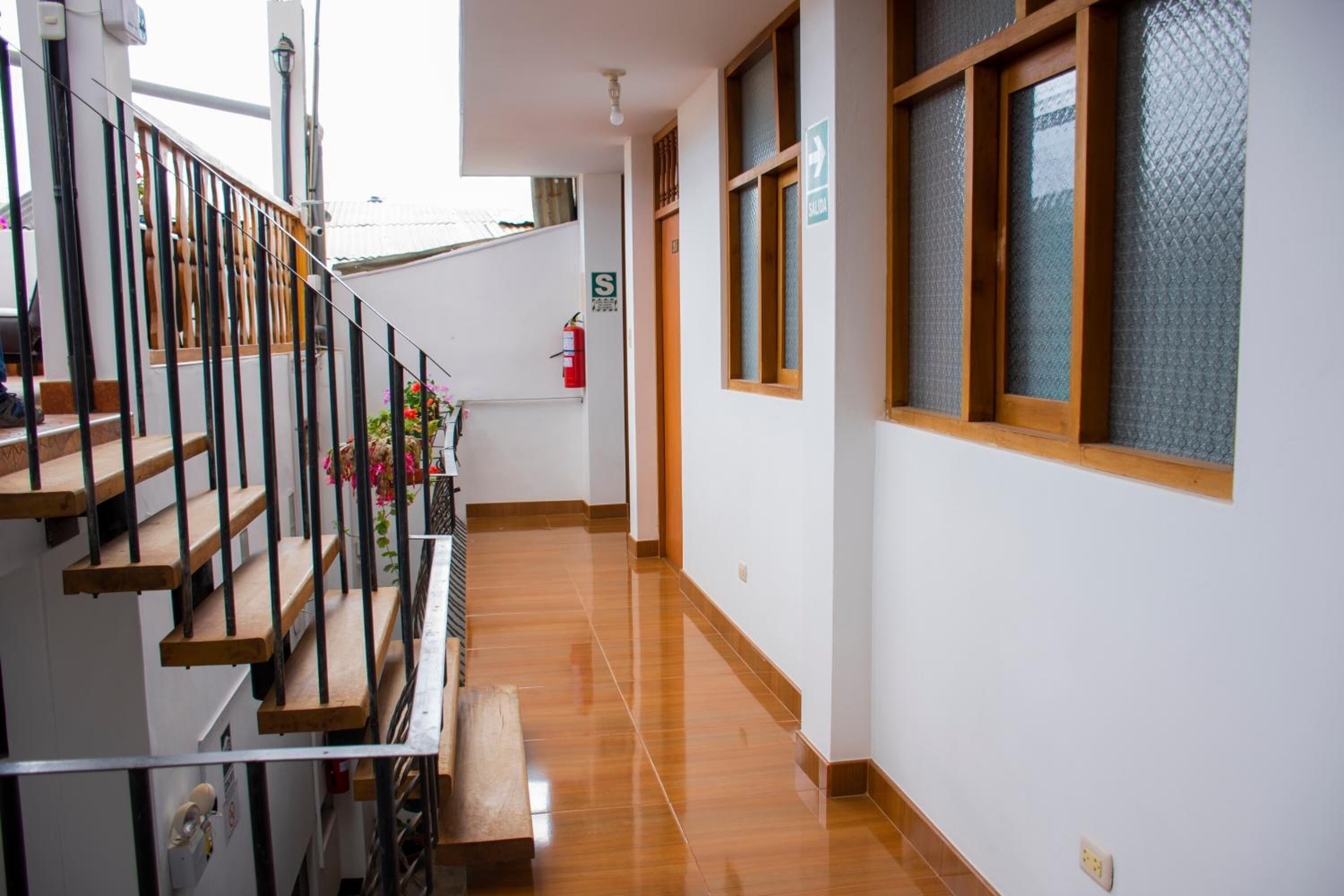 Un couloir avec un plancher en bois, un escalier doté de rampes noires et un extincteur fixé au mur.
