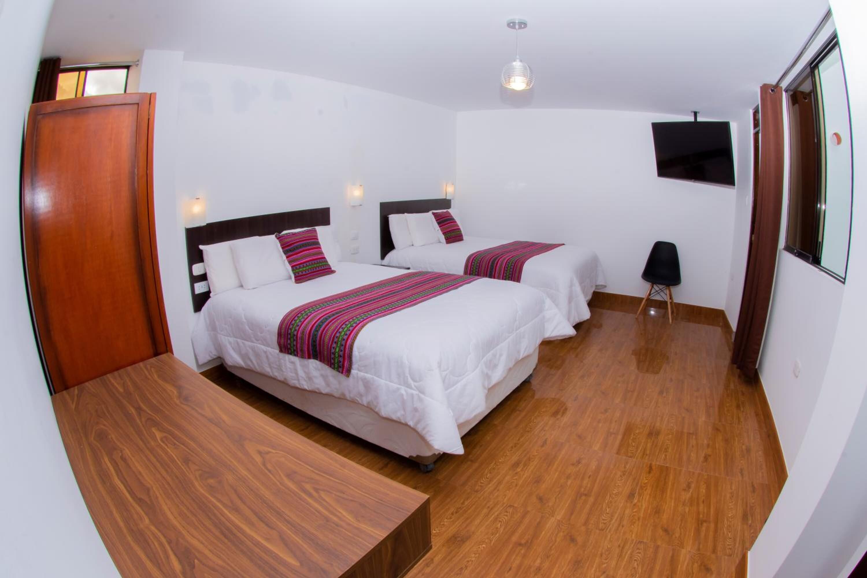 A hotel room with two beds, a wooden desk, a TV, and a window.