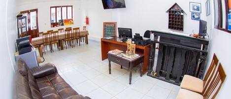 Un hall de hotel con un sofá, zona de comedor, chimenea y televisor montado en la pared.