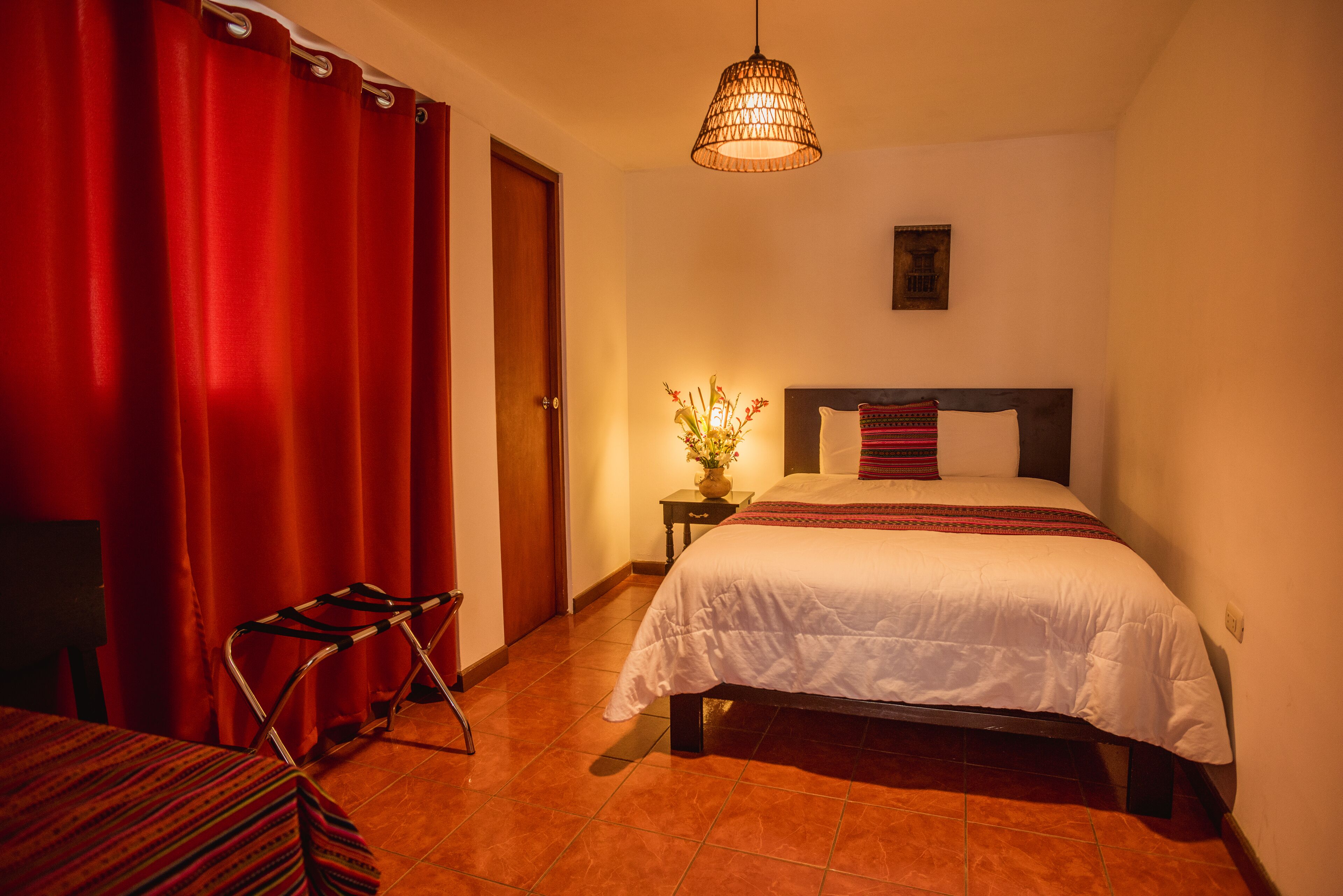 A bedroom with a bed, a nightstand, a lamp, a chair, and a door.