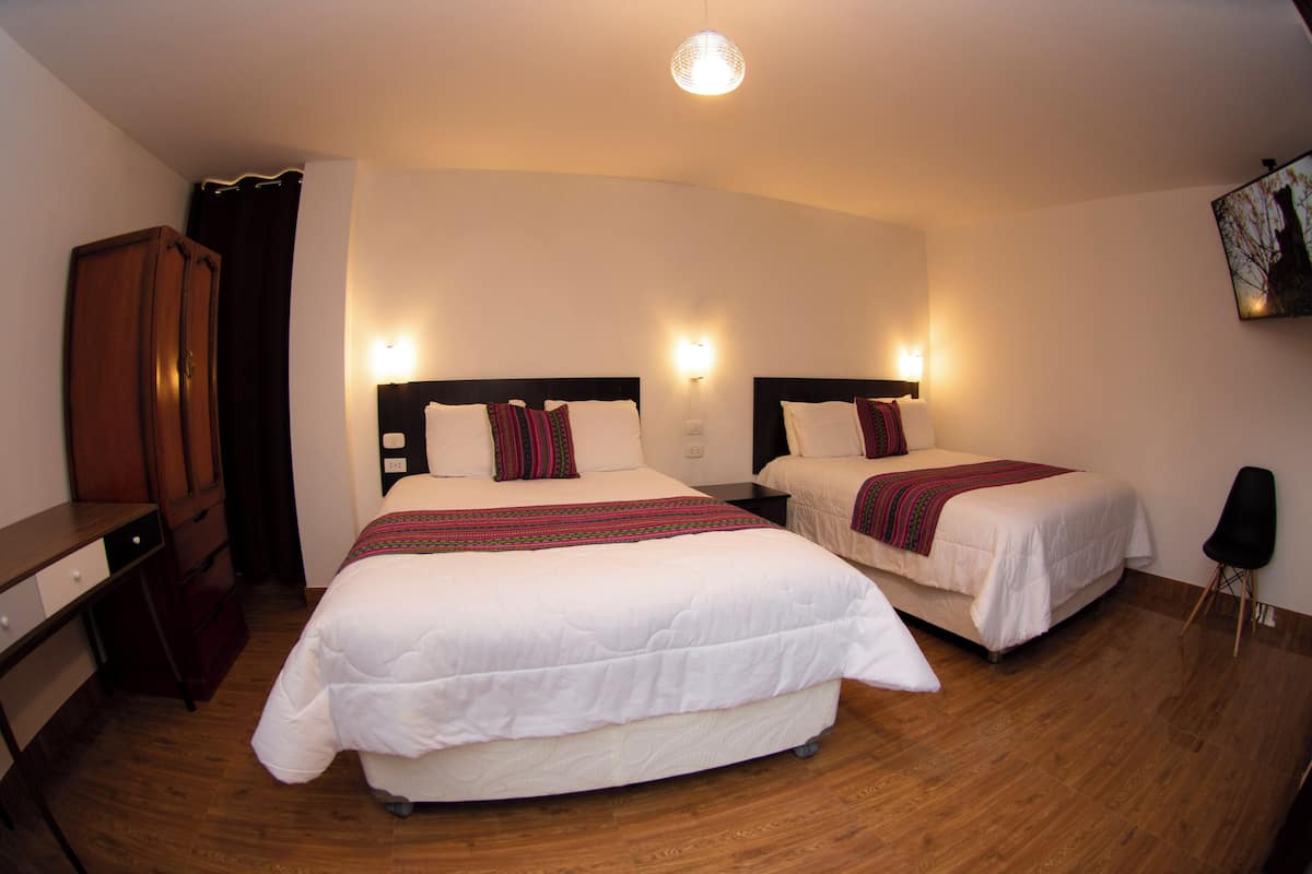Une chambre d’hôtel avec deux lits, un plancher en bois, une armoire et un téléviseur fixé au mur.