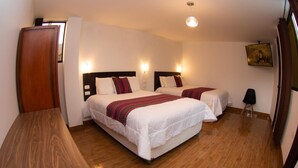 A hotel room with two beds, wooden flooring, a wooden desk, and a painting on the wall.