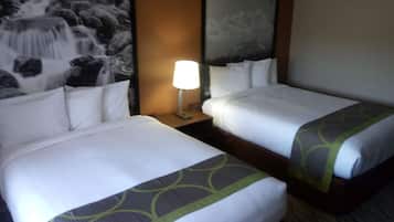 A hotel room with two beds, a nightstand with a lamp, and a painting of a waterfall on the wall.
