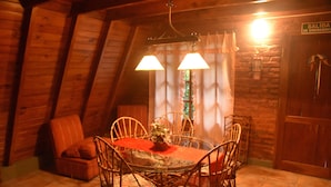 Un comedor de madera con una mesa redonda, sillas y un mantel rojo. Hay un banco de madera y un extintor en la pared.