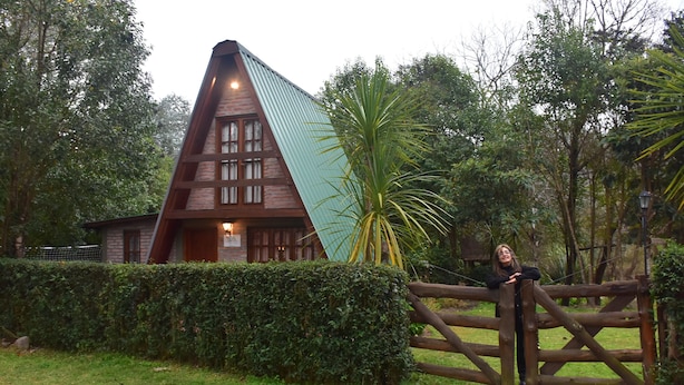 Un edificio triangular con techo inclinado, rodeado por una valla de madera y abundante vegetación.